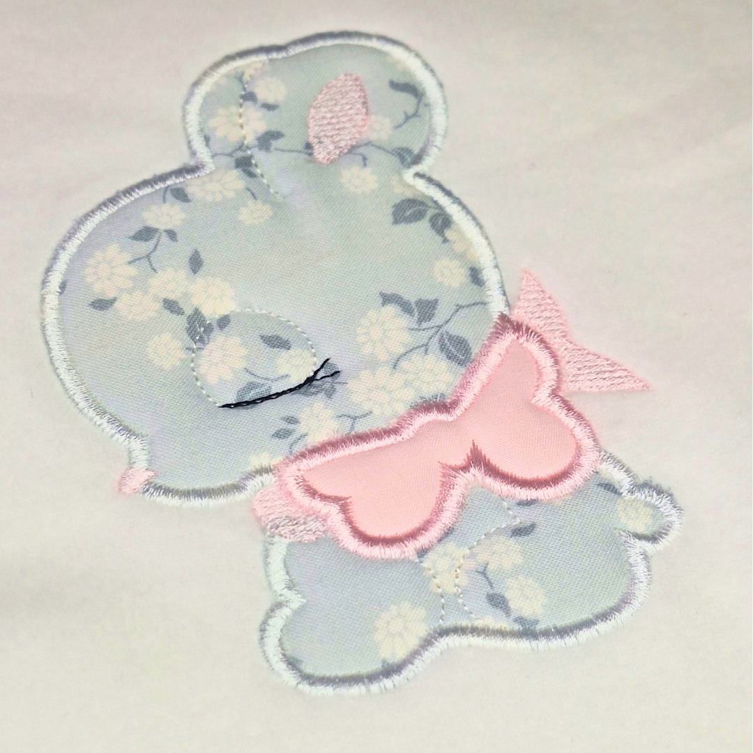 This as an image of an Applique Machine Embroidery Design by Stitches & Strokes, featuring a Baby Bunny with a Pink bow. This adorable baby bunny applique machine embroidery pattern is perfect for embroidery on Easter Decor and Baby Gifts like burp cloths, blankets, crib bedding and travel bags.