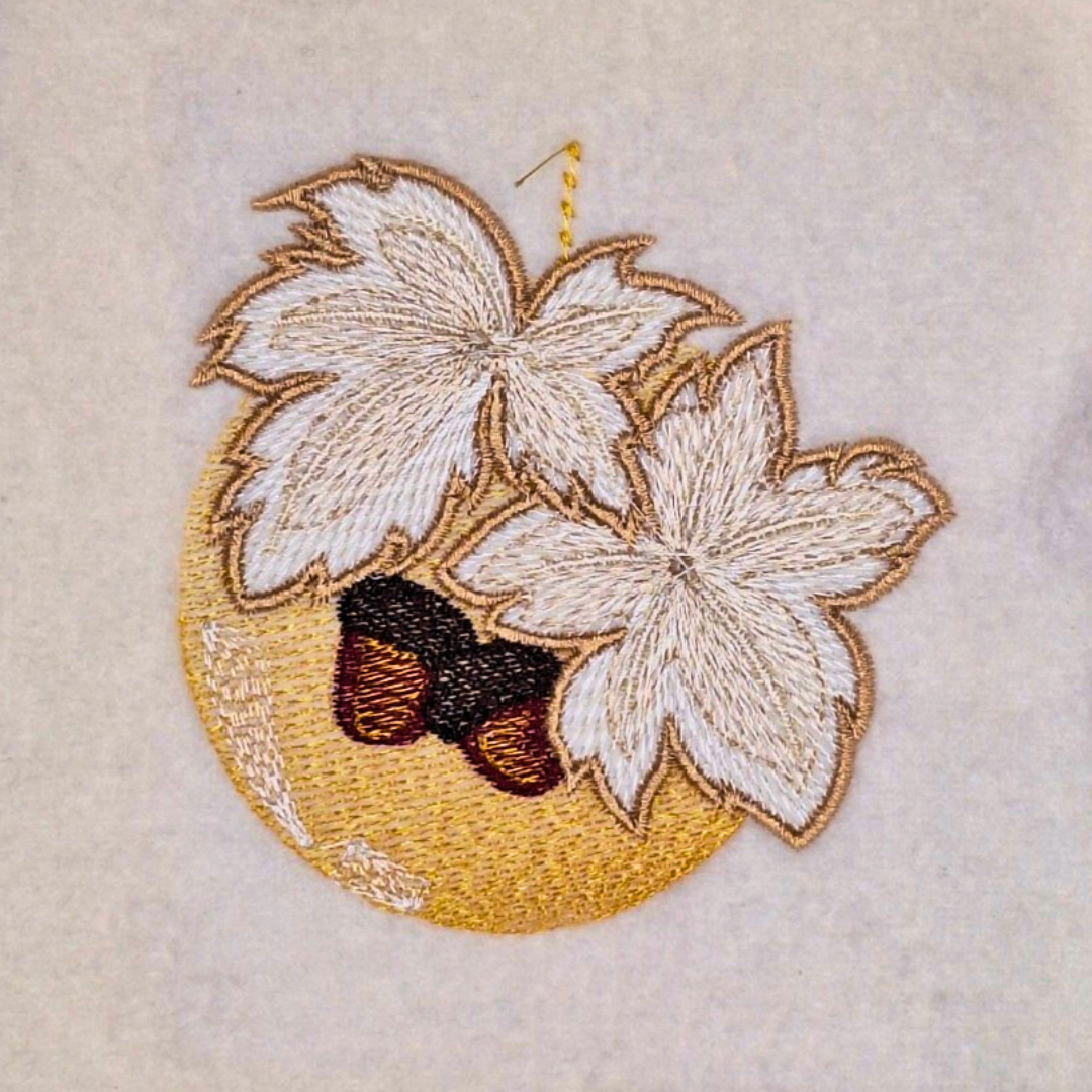 This is an image of a machine embroidery design by Stitches & Strokes, featuring a golden Christmas Ornament adorned with Autumn Leaves in beautiful autumn browns. This Christmas Ornament machine embroidery pattern is perfect for adding some sophistication to your Christmas Décor and Gifts.