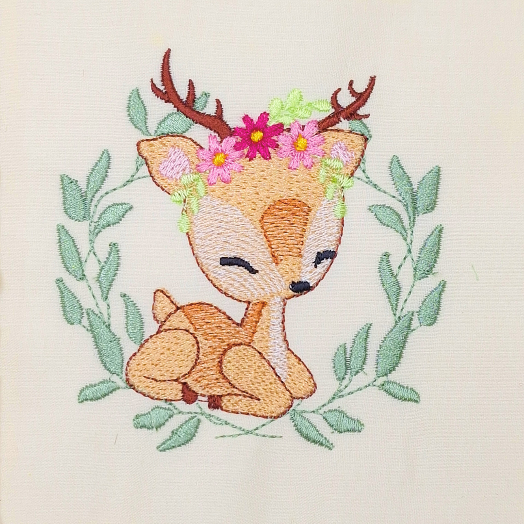 This is an image of a machine embroidery design featuring a baby deer with flowers on it's head and sitting in a leaf wreath. This Baby Deer machine embroidery design is perfect for embroidery on baby burp clothes and onesies for baby shower gifts.