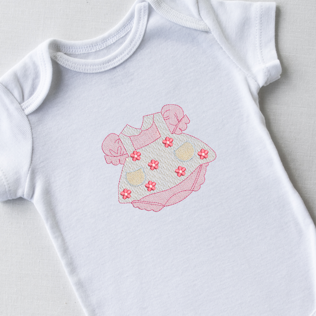 This is an image of a pink and white baby dress machine embroidery design featuring small flowers and little pockets.