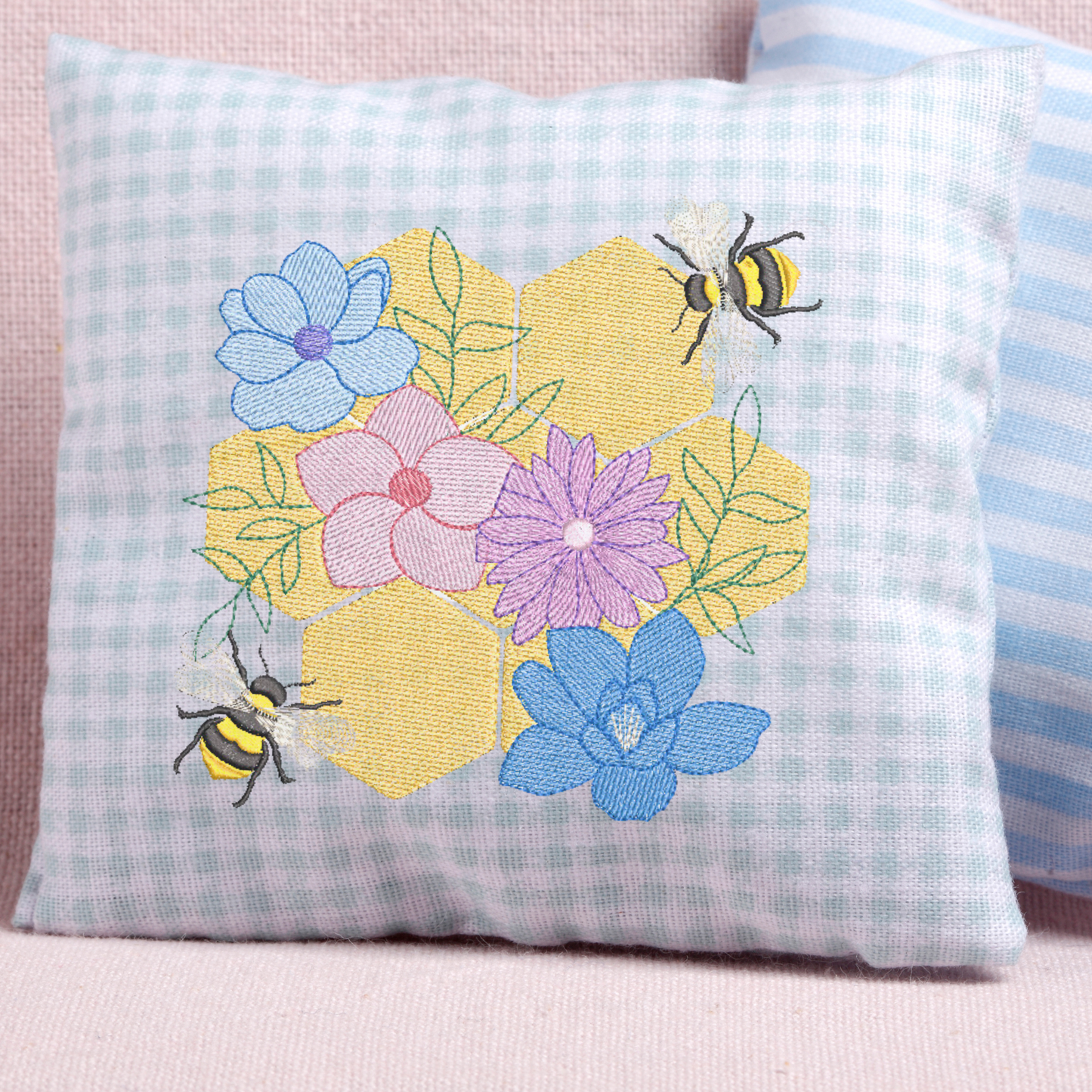 This is an image of a machine embroidery design featuring a honeycomb and two honeybees with beautiful flowers. This honeycomb and bee machine embroidery design is perfect for aprons, tablecloths, and home décor like cushions.