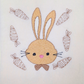 This is an image of a machine embroidery design featuring a cute brown bunny with a heart shaped nose, long ears, and a bow tie. This bunny machine embroidery design is further adorned with cute carrots in an outline stitch. This bunny machine embroidery design from Stitches and Strokes is ideal for embroidery on items for babies like blankets, bibs, and burp cloths, as well as Easter decorations and Easter egg hunt bags.