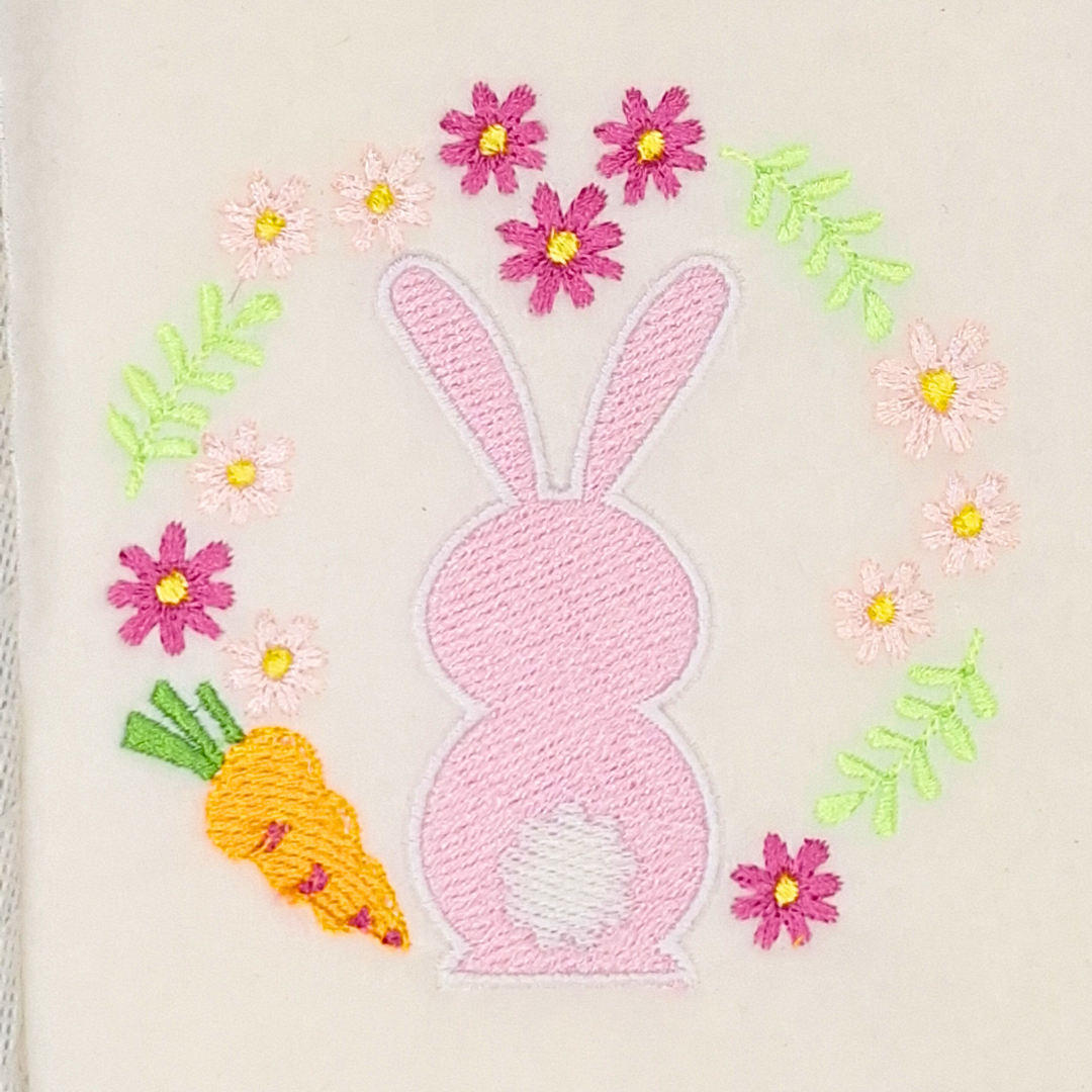 This is an image of a pink Easter bunny with a carrot and flower wreath. This bunny machine embroidery design is perfect for embroidery on items for Easter like décor, gifts, and easter hunt bags.