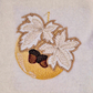 This is an image of a machine embroidery design by Stitches & Strokes, featuring a golden Christmas Ornament adorned with Autumn Leaves in beautiful autumn browns. This Christmas Ornament machine embroidery pattern is perfect for adding some sophistication to your Christmas Décor and Gifts. 