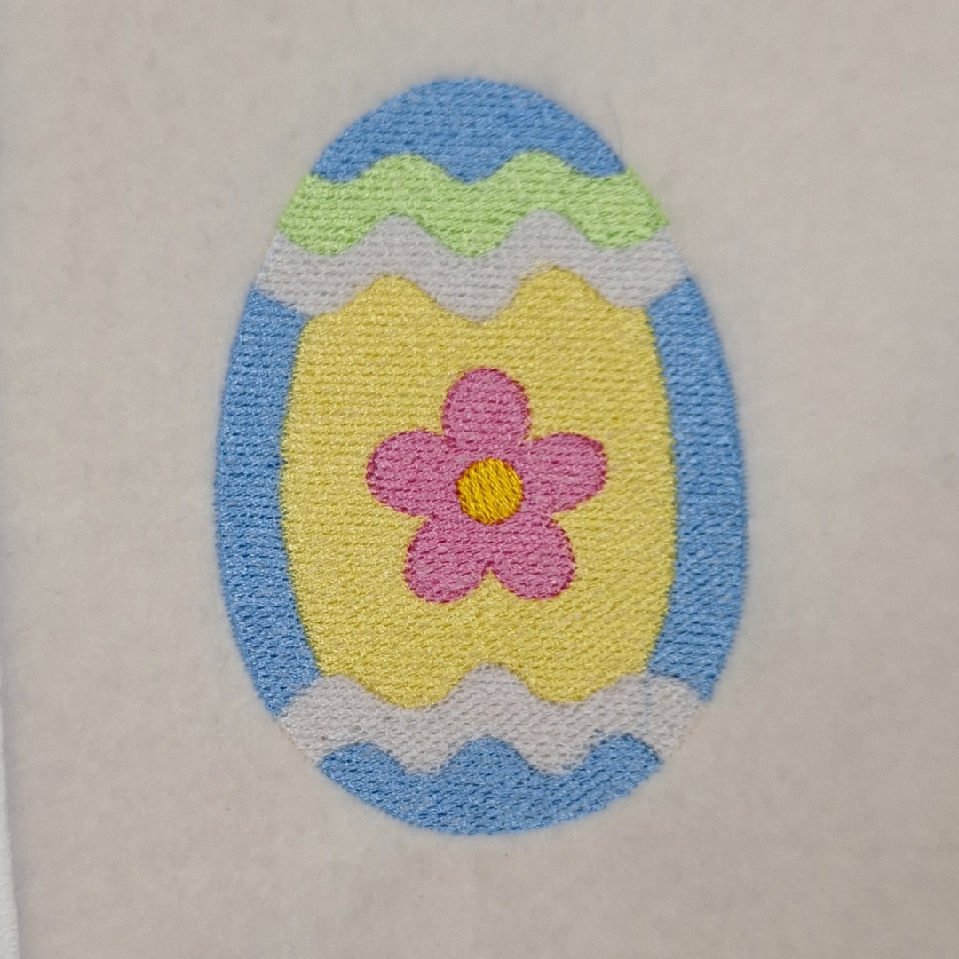 This is an image of an Easter egg in blue and yellow with a pink flower machine embroidery design.