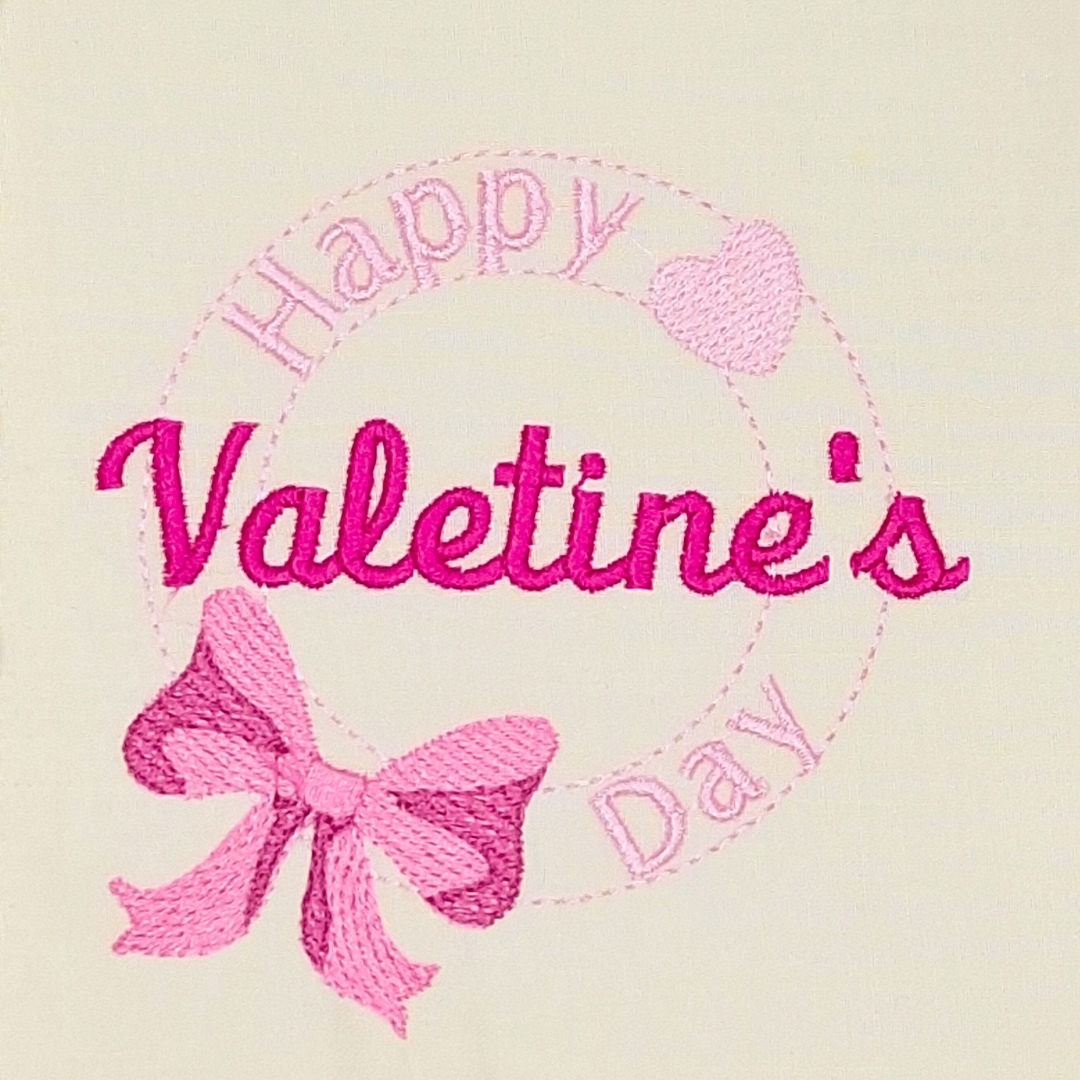 This is an image of a machine embroidery design featuring a circular stamp motif with a cute heart and pink bow with the quote "Happy Valentine's Day.