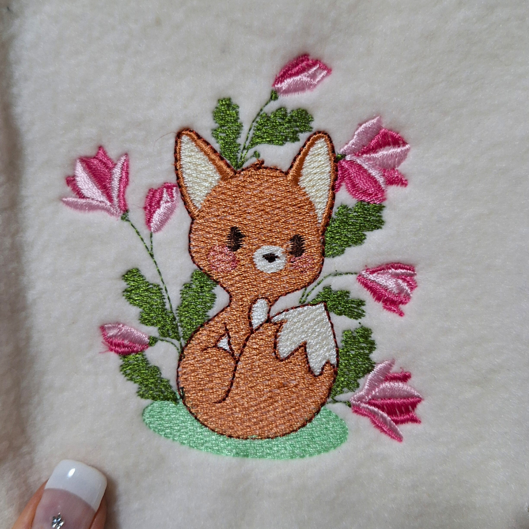 This is a machine embroidery design featuring a cute baby fox, surrounded by delicate magnolia flowers. This adorable baby woodland fox machine embroidery design is available in 4x4, and 5x7 hoop sizes.